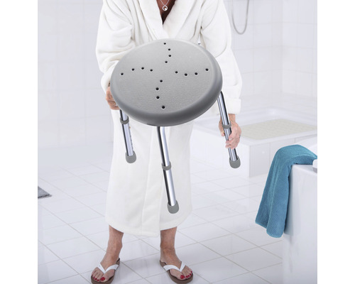 Femme tenant un tabouret de douche avec assise en plastique et pieds en métal dans la salle de bain
