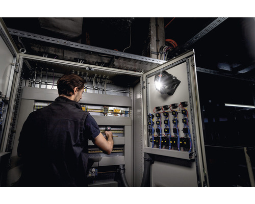 Un homme travaille sur une armoire électrique ouverte avec une lampe de travail