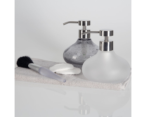 Zwei Seifenspender aus Glas mit Edelstahlpumpe auf einem Handtuch mit Wattestäbchen und Pinsel