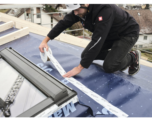 Un homme fixe une fenêtre avec du ruban d''étanchéité sur un toit.
