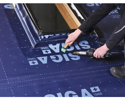 Un artisan travaille une membrane de toit avec un décapeur thermique et un rouleau de pression sur une fenêtre de toit.