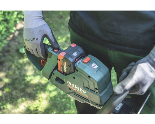 Une personne utilise un taille-haie à batterie Metabo avec batterie