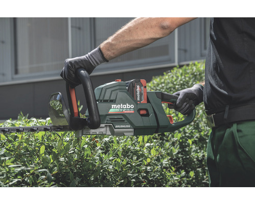 Une personne utilise un taille-haie à batterie Metabo pour tailler une haie.