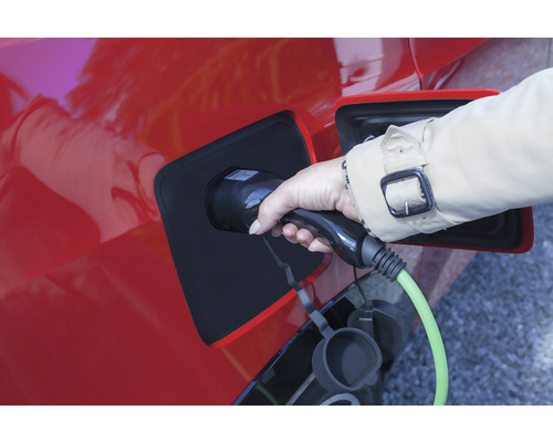 Eine Hand steckt ein Ladekabel in ein rotes Elektroauto.