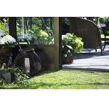 Scène avec une lanterne, un panier de plantes et des meubles de jardin sur une pelouse à côté d''une serre.