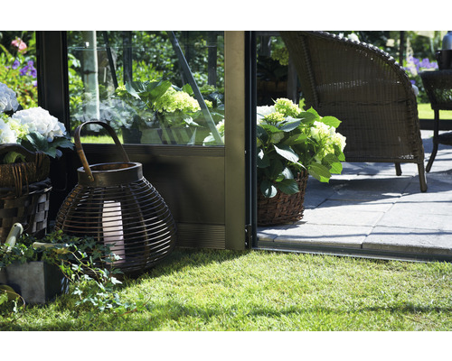 Scène avec une lanterne, un panier de plantes et des meubles de jardin sur une pelouse à côté d''une serre.