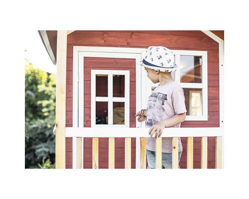 Enfant devant une cabane de jeu en bois rouge avec des détails blancs