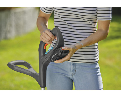 Eine Person befestigt einen Akku an einem Rasentrimmer.