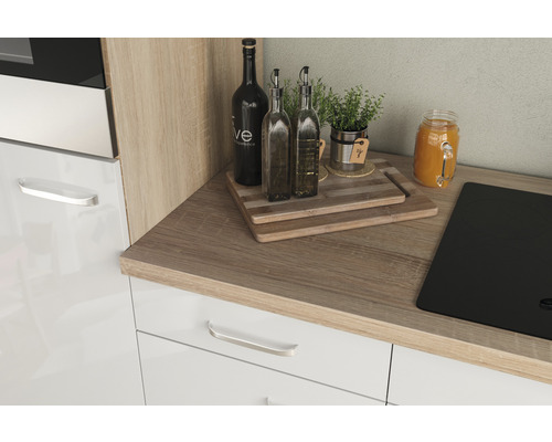Plan de travail de cuisine avec plaque de cuisson, bouteilles, herbes aromatiques et planches à découper