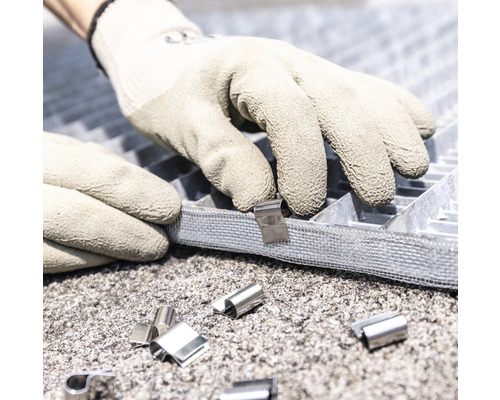 Des mains gantées fixent un rail métallique sur une grille.