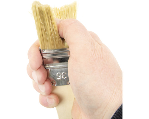 Main tenant un pinceau avec un manche en bois et des poils