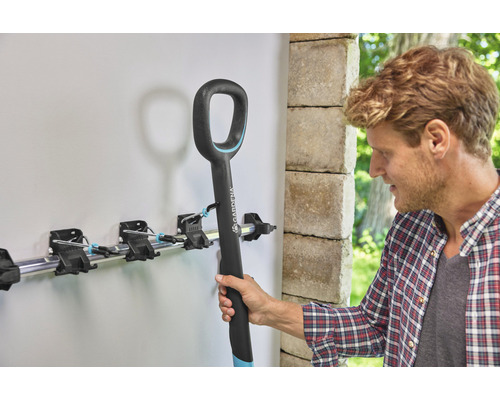 Un homme accroche un outil de jardin dans une barre porte-outils