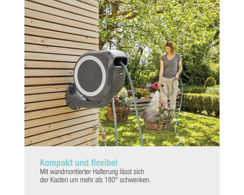 Gartenszene mit Schlauchbox an einer Holzwand und einer Frau, die Blumen giesst