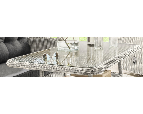 Gros plan d''une table de jardin en rotin avec un plateau en verre, sur laquelle sont posées des lunettes de soleil et un vase.