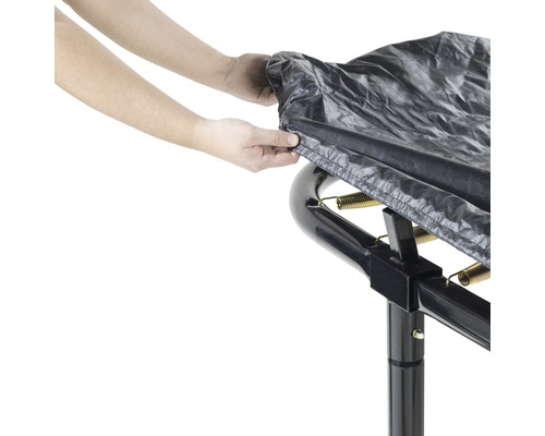 Une personne fixe une housse de protection sur un trampoline de jardin.