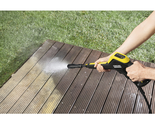 Une personne nettoie une terrasse en bois avec un nettoyeur haute pression Kärcher.