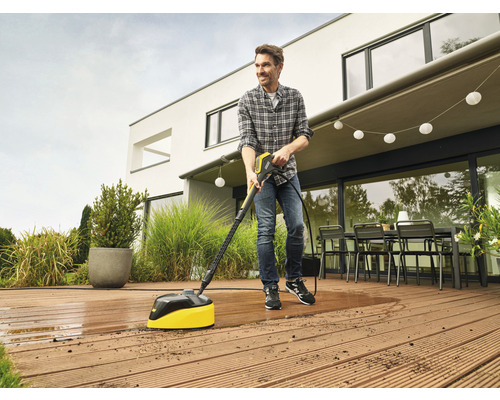 Un homme nettoie une terrasse en bois avec un nettoyeur de terrasse.