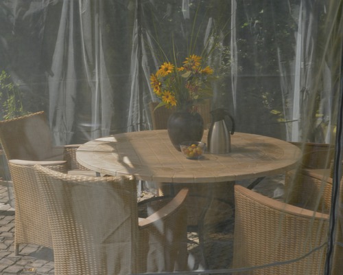Table de jardin ronde avec chaises et décoration sous une couverture transparente.