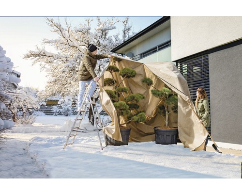 Des personnes protègent des plantes avec une housse de protection hivernale dans le jardin