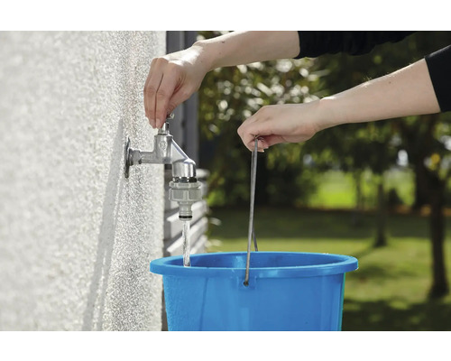 Une personne remplit un seau bleu avec de l''eau provenant d''un robinet extérieur.