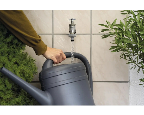 Une personne remplit un arrosoir gris avec de l''eau d''un robinet de jardin.