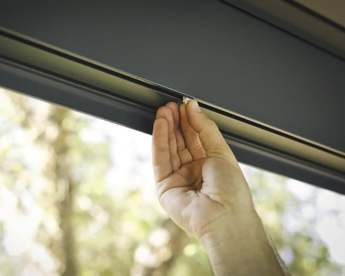 Une main fixe une fermeture sur un store enrouleur