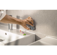 Person befestigt Badaccessoire an Wandfliesen im Badezimmer.