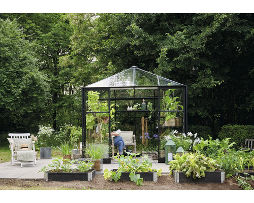 Gartenszene mit Gewächshaus, Hochbeeten, Stuhl und Person