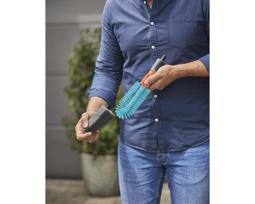 Mann hält Reinigungsbürste und Schwamm für die Gartenbewässerung.