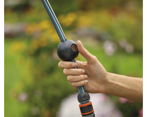 Une main actionne un tuyau d''arrosage flexible avec débit d''eau réglable