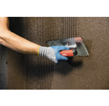 Handwerker trägt mit einer Zahnspachtel Kleber auf eine Wand auf.