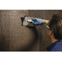 Handwerker trägt Fliesenkleber mit einer Glättkelle auf eine Wand auf.