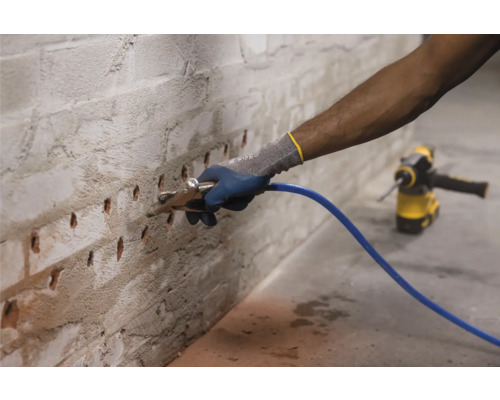 Mann spritzt Injektionsmittel in eine Ziegelwand mit Bohrlöchern zur Mauertrockenlegung.