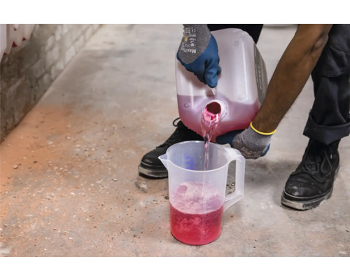 Eine Person giesst Flüssigkeit aus einem Behälter in einen Messbecher.