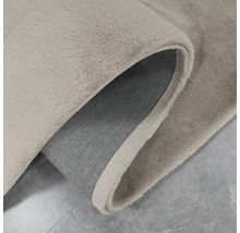 Vue détaillée d''un tapis beige avec un coin retroussé, montrant la texture et le dessous