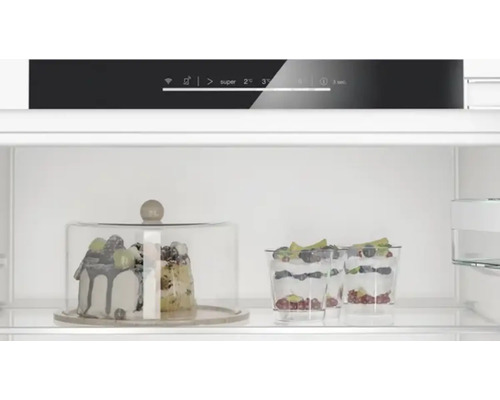 Innenraum eines Kühlschranks mit Kuchen unter einer Glasglocke und Desserts im Glas