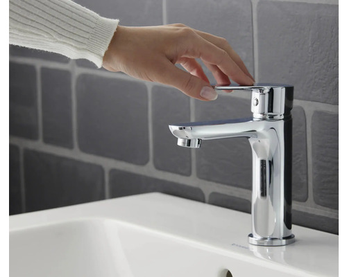 Une main actionne un mitigeur de lavabo chromé sur un lavabo.