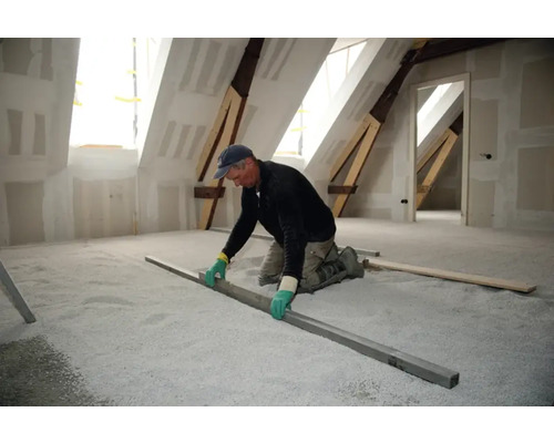 Un artisan nivelle un matériau de remplissage égalisateur dans un grenier avec une règle.