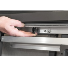 Detailaufnahme einer Hand, die eine schwarze Halteklammer an einer Fensterschiene befestigt.