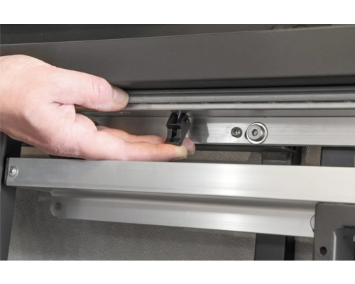 Detailaufnahme einer Hand, die eine schwarze Halteklammer an einer Fensterschiene befestigt.