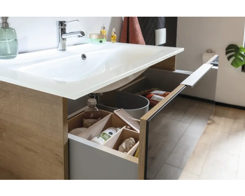 Meuble-lavabo de salle de bains avec tiroir ouvert montrant des produits cosmétiques et un seau