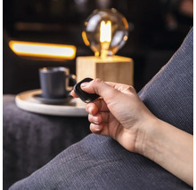 Eine Person bedient eine Fernbedienung in einem Wohnzimmer mit Lampe und Tasse.