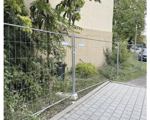 Bauzaun vor einem Gebäude mit Vegetation