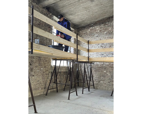 Un homme travaille avec une perceuse sur une structure en bois posée sur des tréteaux.