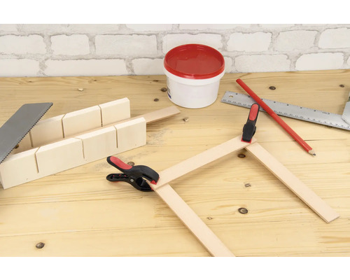 Werkbank-Szene mit Gehrungssäge, Metallsäge, Holzleisten, Schraubzwingen, Bleistift, Metallwinkel und Farbdose.