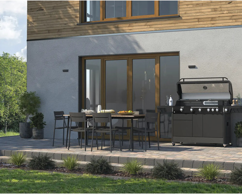 Terrasse avec table à manger, chaises et barbecue à gaz devant une maison.