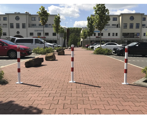 Trois bornes de sécurité à rayures rouges et blanches sur des pavés