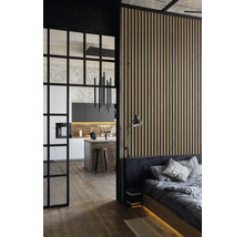 Blick in ein modern eingerichtetes Schlafzimmer mit Holzwand, angrenzender Küche und schwarzer Glastür