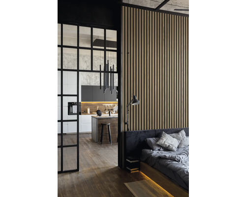 Blick in ein modern eingerichtetes Schlafzimmer mit Holzwand, angrenzender Küche und schwarzer Glastür