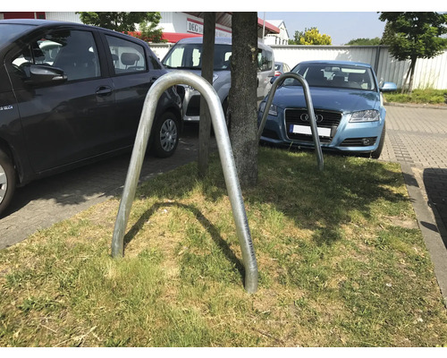 Deux range-vélos en métal en forme de U sur une pelouse devant des voitures en stationnement.